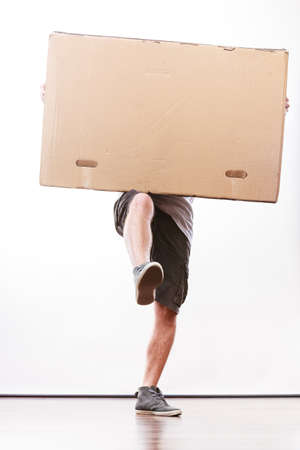 Removal service and delivery concept. Young male guy postal courier holding big very heavy cube package carton.の写真素材