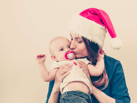Family celebration concept. Christmas woman with cute baby. Beautiful lady has red santa claus cap.の写真素材