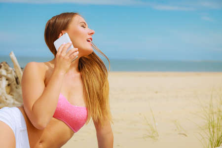 Technology and communication. Happy smiling woman with mobile phone calling to people friends. Young attractive girl talking by smartphone on beach.の写真素材