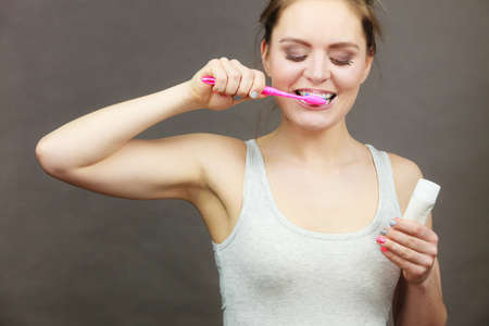 Woman holding brush and tooth paste for teeth cleaning. Happy funny smiling girl with toothbrush. Oral hygiene. Studio shot dark backgroundの写真素材