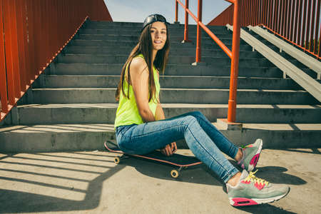 Cool young long haired girl sitting on skateboard near the urban stairs. Active lifestyle funky in summer. Trendy sport teen.の写真素材