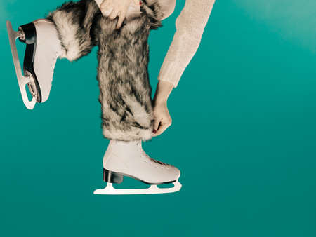 Woman legs wearing skates fur warm socks. Girl getting ready for ice skating. Winter sport activity. Studio shot on blue greenの写真素材