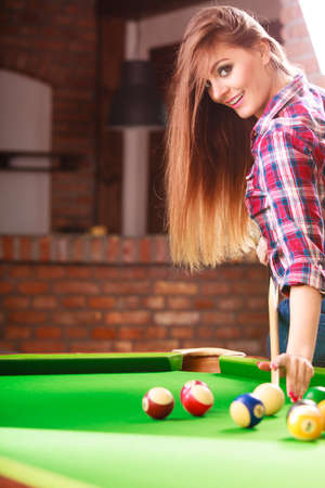 Play and fun concept. Young happy girl having fun with billiard. Smiling fashionable woman playing...