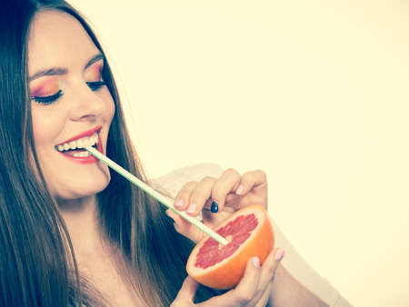 Woman attractive long hair girl eyes makeup holding grapefruit citrus sipping juice from fruit. Healthy diet food. Summer vacation holidays concept. Toned imageの写真素材