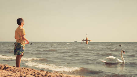 Water fun and joy outside. Little boy walking through the sea ocean. Lonely kid playing outdoors in summer clothes.の写真素材