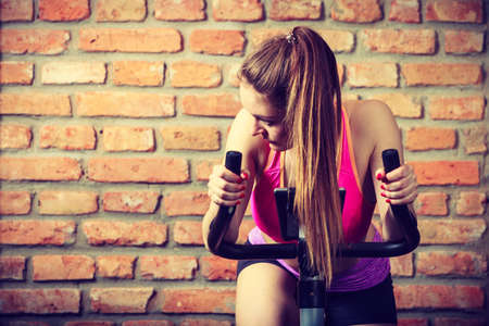 Active woman wearing sport bra working out,  using exercise bike at the gym. Sporty girl training in fitness center. Slim body weight loss concept.の写真素材
