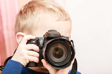 Technology and childhood. Discovering and fun. Child play and take photo in home. Boy wear blue shirt and hold camera.の写真素材