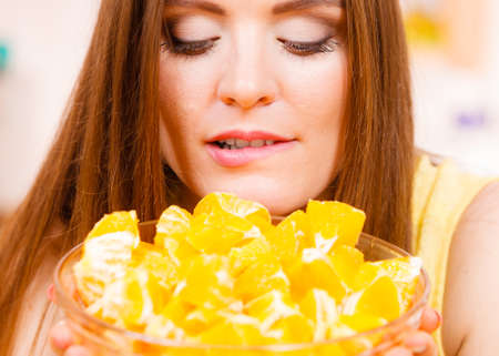 Woman young housewife in kitchen holds bowl full of sliced orange fruits preparing to make fresh juice or salad. Healthy eating, cooking, vegetarian food, dieting and people concept.の写真素材