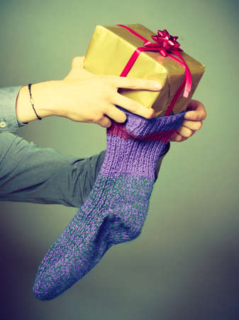 Holiday, xmas winter time season. Male hands putting wrapped gift in knitted christmas sockの写真素材