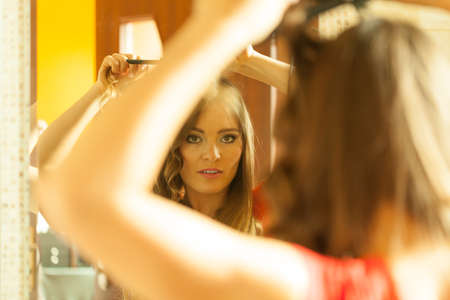 Hairstyles concept. Gorgeous woman with elegant make up making beauty hairdo curls on long straight dark hair. Reflection in mirror.の写真素材