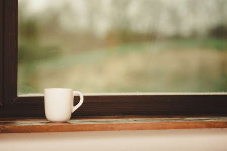 White single tea or coffee mug on window sill.の写真素材