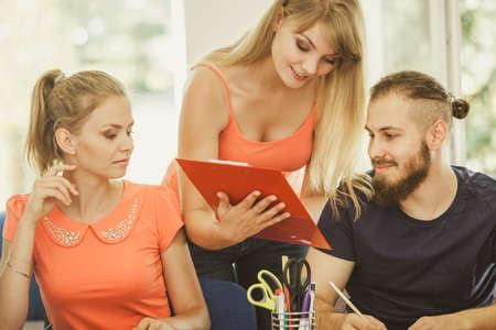 Teaching Concept. Female young teacher or tutor with adult students in classroom with papers, laptop...