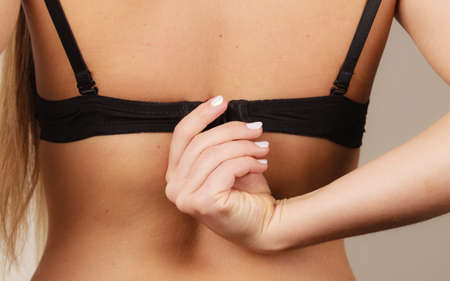 Woman back view putting on or taking off black bra lingerie. Bosom concept. Attractive female dressing up.の写真素材