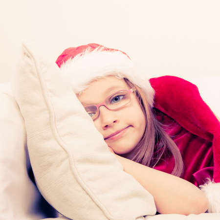 Girl family time during christmas. Cute little lady crawling on sofa. Small woman lying on the couch. Resting time wearing red santa claus hat and shoes.の写真素材