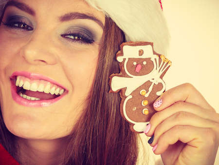 Woman wearing red hat holding delicious sweet gingerbread xmas cookie little snowman. Happy girl awaiting christmas holidays, close upの写真素材