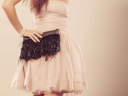 Beauty, fashion and elegant people concept - slim woman in bright dress holds clutch bag in hand, part of body female waistlineの写真素材