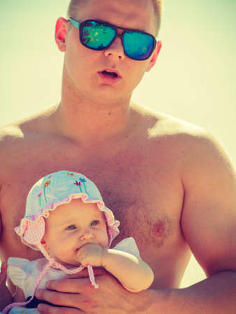 Father holding baby posing in swimsuits on sunny dayの写真素材