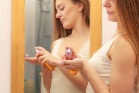 Woman in bathroom holding bottle with cosmetic oil. Girl taking care of her long smooth hair...
