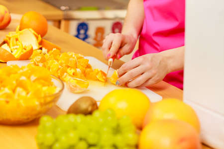 Woman young housewife in kitchen at home slicing fresh orange fruits on cutting board for salad or juicing. Healthy eating, cooking, raw food, dieting and people concept.の写真素材