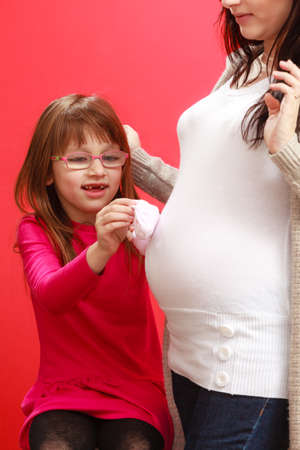 Pregnancy, motherhood, family concept. Pregnant woman with her daughter holding little white baby...