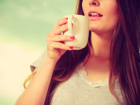 Morning, drink concept. Beautiful smiling young woman holding and drinking a cup of hot coffee or...