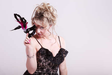 Party time, holidays, people and celebration concept. Woman middle aged blonde female holds carnival mask. Lady wearing elegant black dressの写真素材