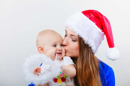Christmas family holiday concept. Mother wearing santa claus hat holding, hugging and kissing baby.の写真素材