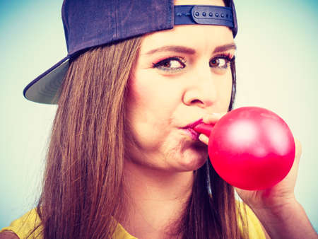 Teens and parties. Preparation for celebration. Trendy teenage girl blowing red balloon. Young beauty woman prepare accessories for party.の写真素材