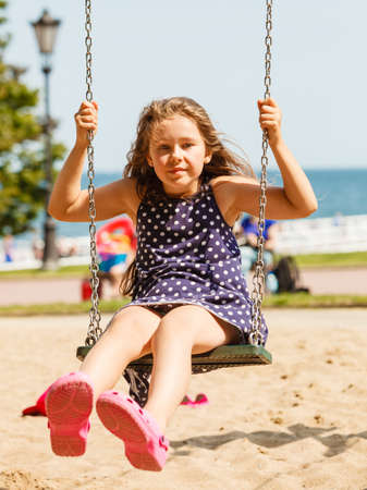 Have fun and leisure concept. Long haired enjoyable girl swinging outdoor in garden playground. Lovely child playing on swing-set.の写真素材