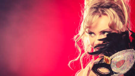 Party entertainment time concept. Woman with carnival mask. Lady wearing elegant blak dress, she has blonde hair.の写真素材
