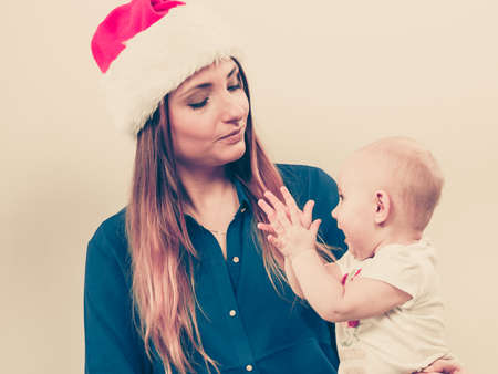 Christmas family holiday concept. Mother wearing santa claus hat holding and hugging baby.の写真素材