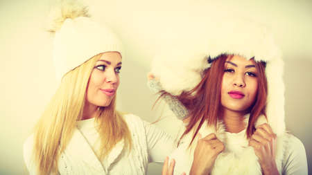 Clothing people fashion concept. Two ladies in winter outfit. Blonde woman together with mulatto girl, wearing white warm clothes.の写真素材