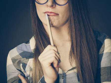 Woman confused thinking seeks a solution, paper card with question mark on her head. Doubtful young female in glasses studio shot on blackの写真素材