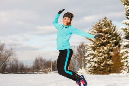 Winter fun people concept. Young girl jumping in the snow. Attractive lady wearing blue jumper and sporty leggins.の写真素材