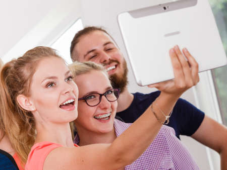 Fun bonding selfie concept. Group of diverse friends students classmates taking self photo with tablet pc computer indoors in classの写真素材