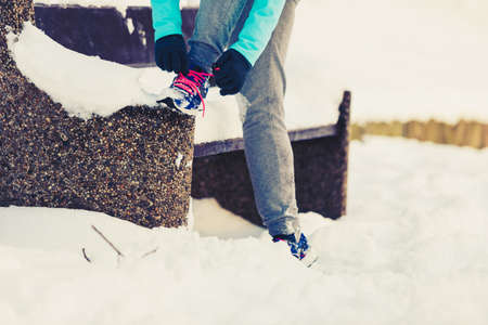 Exercising girl tying sholeaces. Young female in park. Fitness outdoors fashion shoes concept.の写真素材
