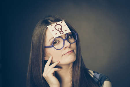 Woman confused thinking seeks a solution, paper card with light idea bulb on her head. Student girl looking for new ideas. Eureka creativity conceptの写真素材