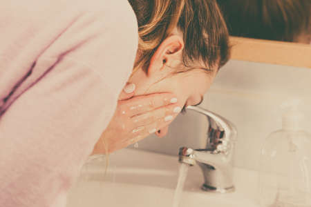 Woman cleaning washing her face with clean water in bathroom. Girl taking care of her complexion. Morning hygiene. Skincare treatmentの写真素材