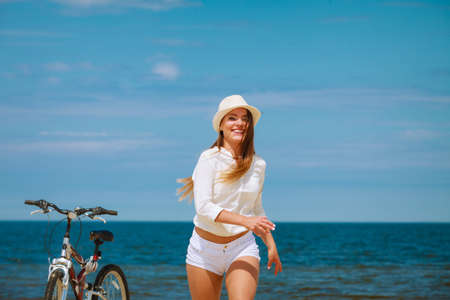 Sport and recreation. Young girl in straw hat resting after cycling on beach. Smiling tourist...