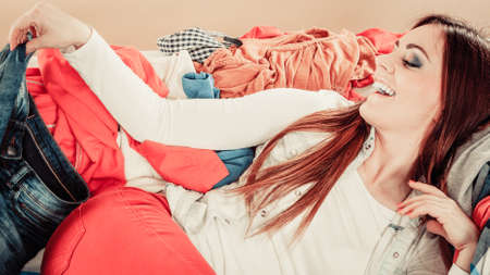 Lifestyle and decisions about outfit. Young female lie on sofa full of colorful clothes. Smiling woman surrounded by garment.の写真素材