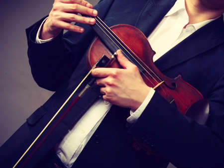 Music passion, hobby concept. Man man dressed elegantly holding wooden violin. Studio shot on dark backgroundの写真素材