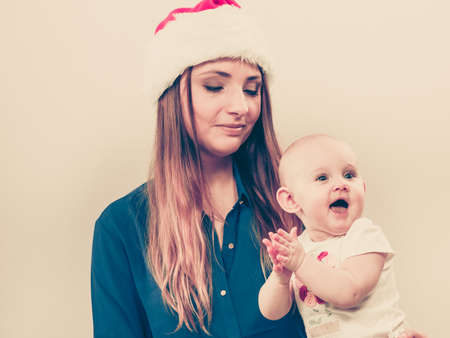 Christmas family holiday concept. Mother wearing santa claus hat holding and hugging baby.の写真素材