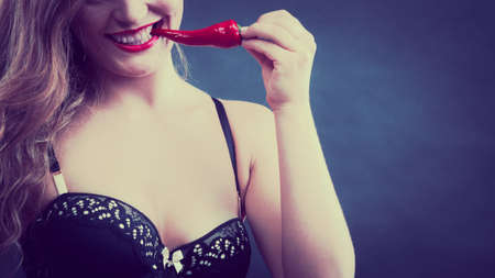 Sensual seductive attractive woman wearing lingerie biting chilli pepper. Erotic, fashion concept, half faceの写真素材