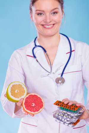 Dietitian nutritionist woman holding diet weight loss tablets pills and grapefruits. Choice between natural and synthetic way of slimming dieting. Health care.の写真素材