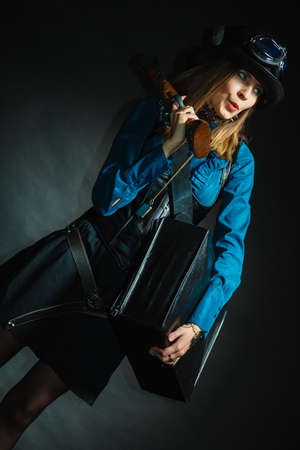 Steampunk subculture weapon threat concept. Vintage girl with gun. Young attractive lady in elegant outfit holding antique firearm.の写真素材
