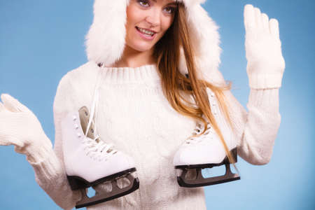 Sport, winter, people concept. Beautiful lady with two skates. Girl is wearing white gloves and fur cap.の写真素材