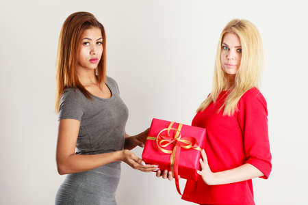 Occasions gifts people concept. Beautiful women blonde caucasian girl and mulatto with red gift box...