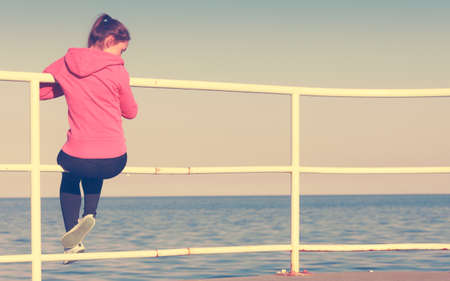 Woman resting after doing sports outdoors. Fitness girl in sportswear sitting on pier relaxing looking at horizon back viewの写真素材