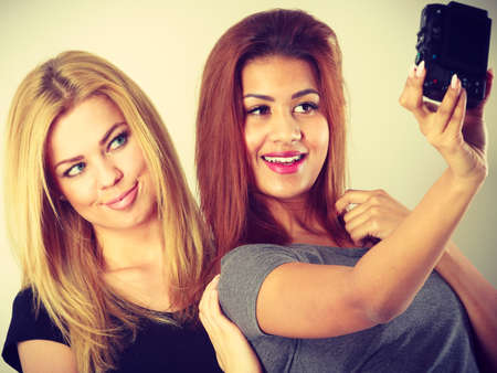 Technology internet and happiness concept. Young women blonde and mixed race taking self picture selfie with cameraの写真素材