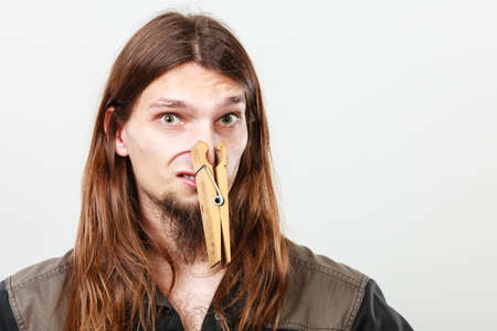 Unpleasant bad smell concept. Portrait of young long haired man with clogged nose by big clothespin.